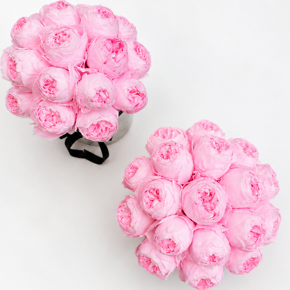 Two round clusters of light pink artificial flowers arranged on a plain white background, with one bouquet in a metallic container and the other loose.