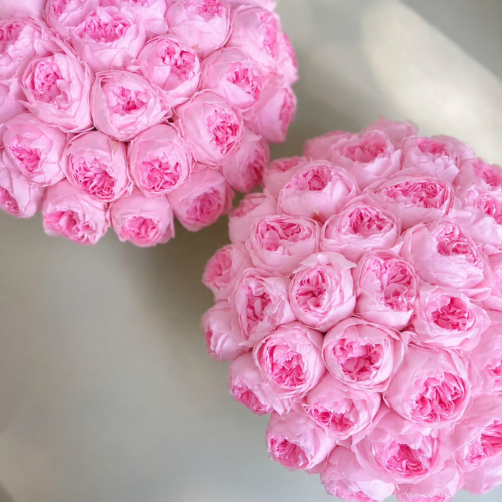 Two round arrangements of light pink artificial roses, photographed on a soft light gray background.