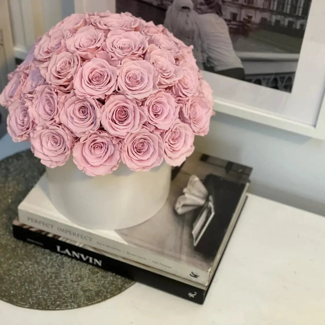Bouquet of pink roses in a white vase on top of a black book with 'LANVIN' branding.