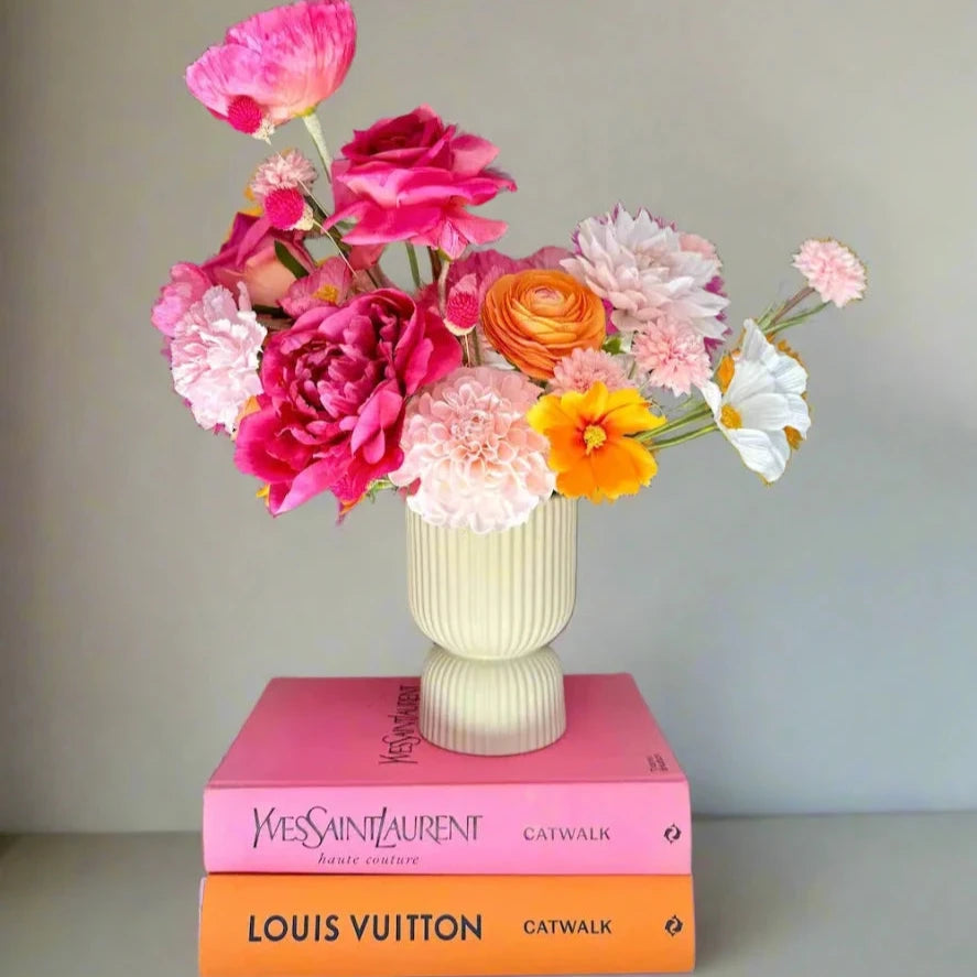 Colorful flower arrangement in a vase on top of two books with visible brand names.