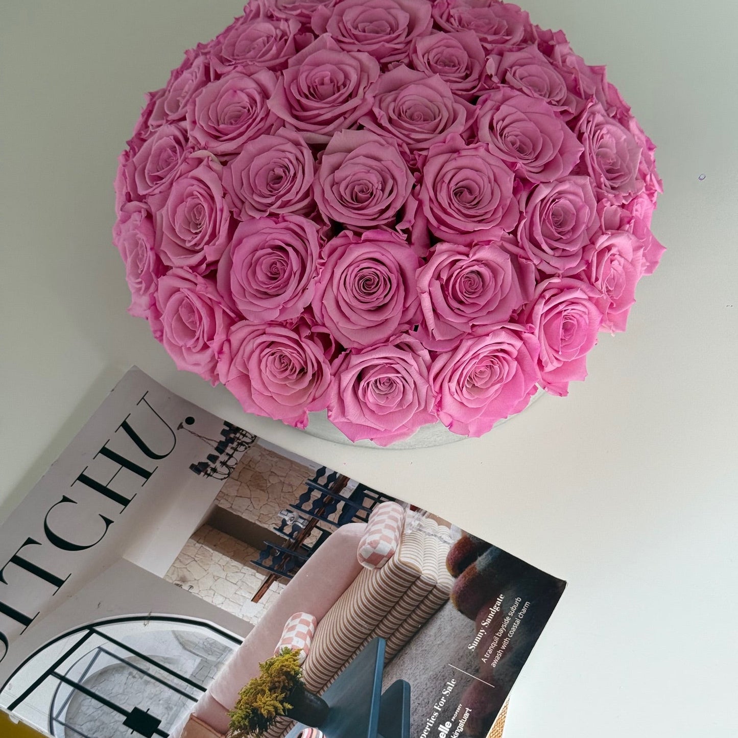 Everlasting roses in cement pot styled with magazines on white table.