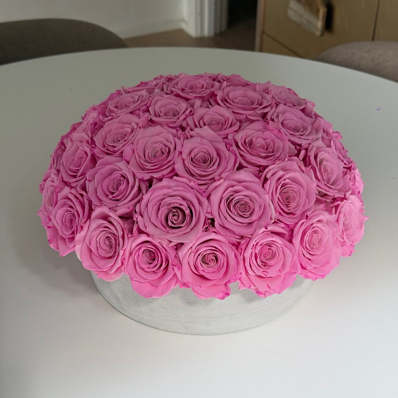 Preserved pink roses in cement pot under warm dining light.