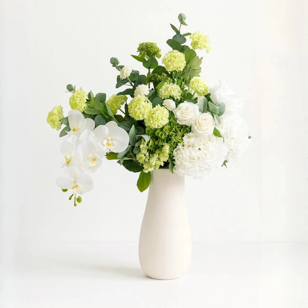 Bouquet of white and green flowers in a white vase on a light background