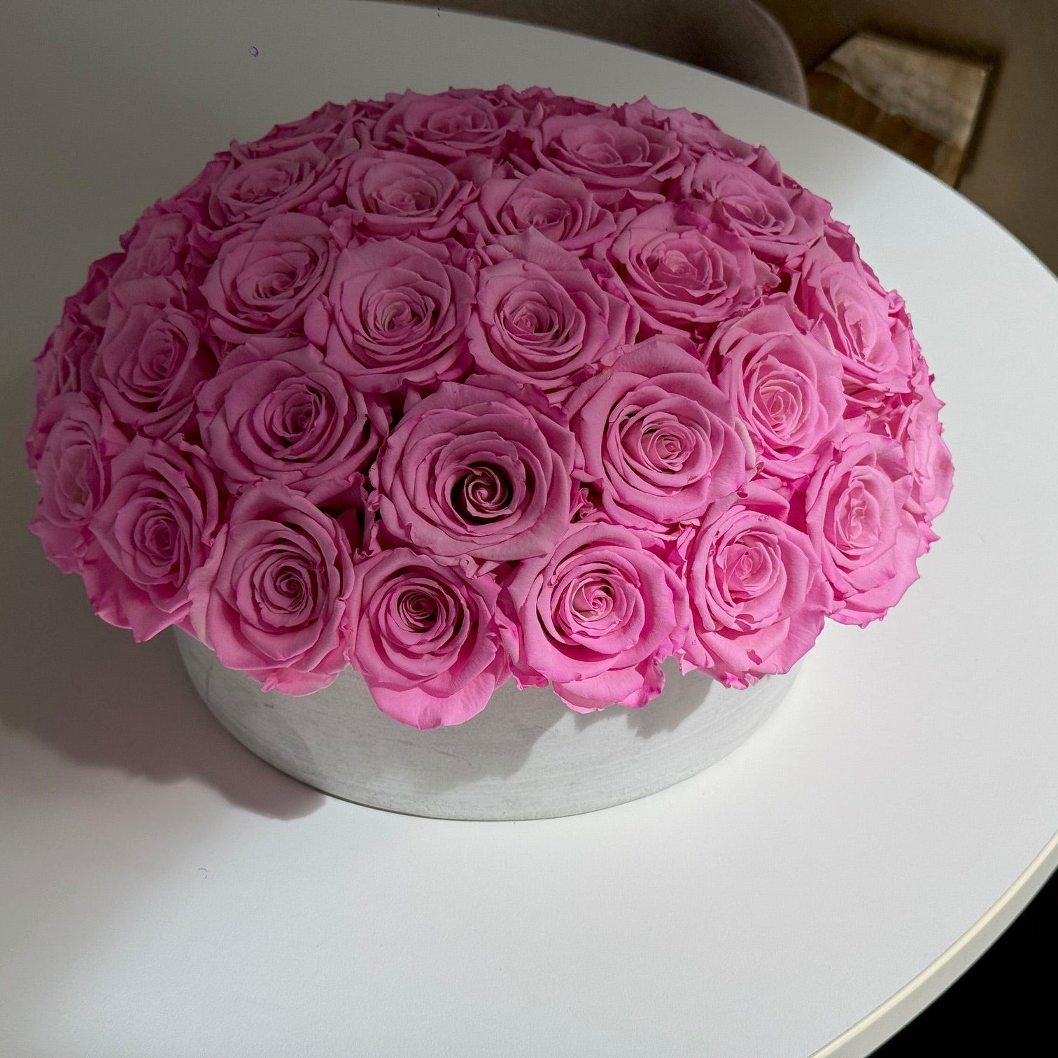 Preserved pink roses in cement pot near window with natural light.