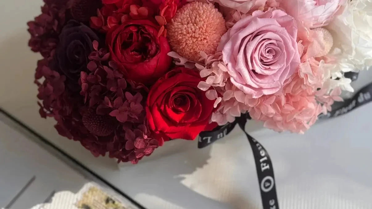 Bouquet of red, pink, and white flowers with a black ribbon on a white surface.