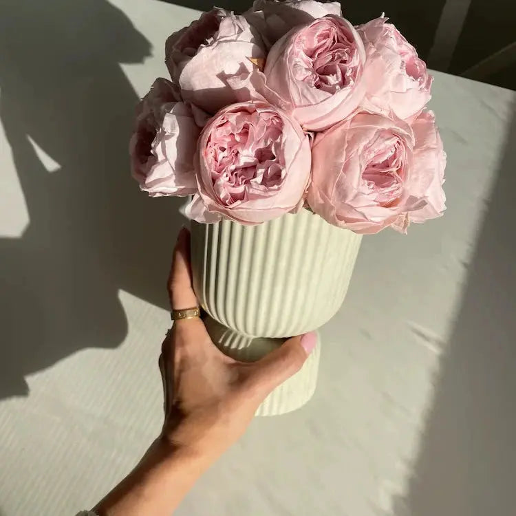 Hand holding a vase with pink flowers on a light surface
