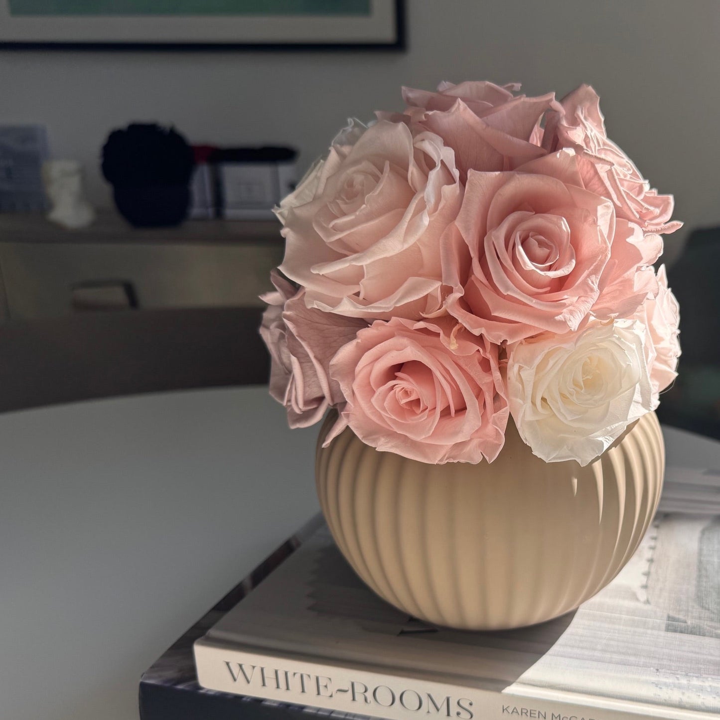 Close-up view of meticulously preserved cream-colored roses arranged in a ribbed sand-colored pot