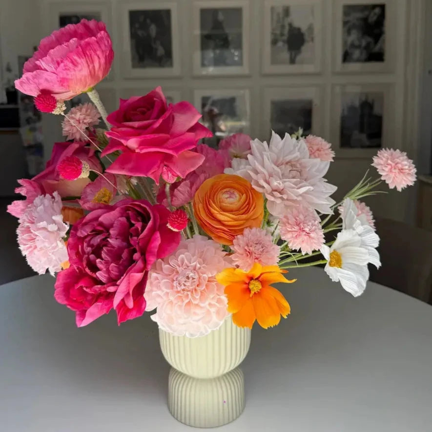 Bouquet of colorful flowers in a vase on a table with a wall of framed pictures in the background.