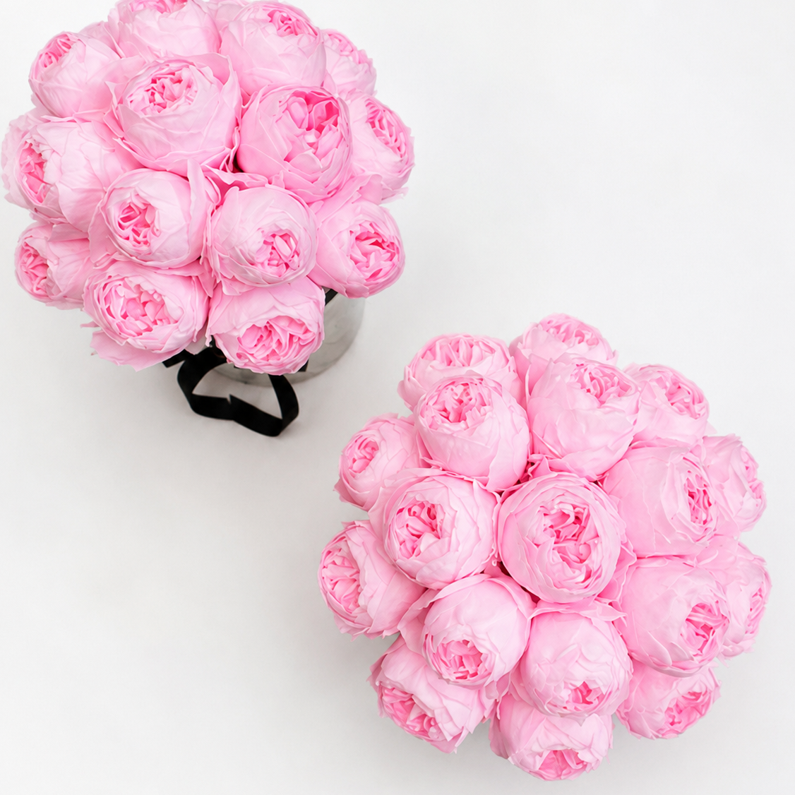 Two round clusters of light pink artificial flowers arranged on a plain white background, with one bouquet in a metallic container and the other loose.