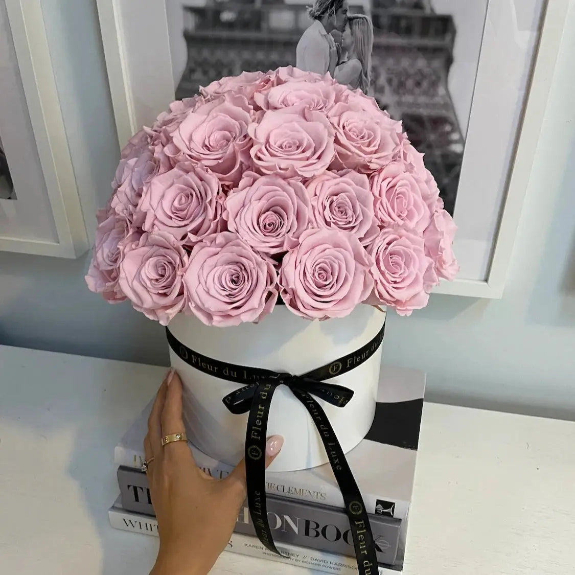 Bouquet of pink roses in a white vase with a black ribbon on a table.