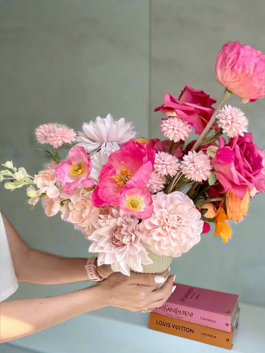 Person holding a vibrant bouquet of flowers with a Louis Vuitton book in the background.