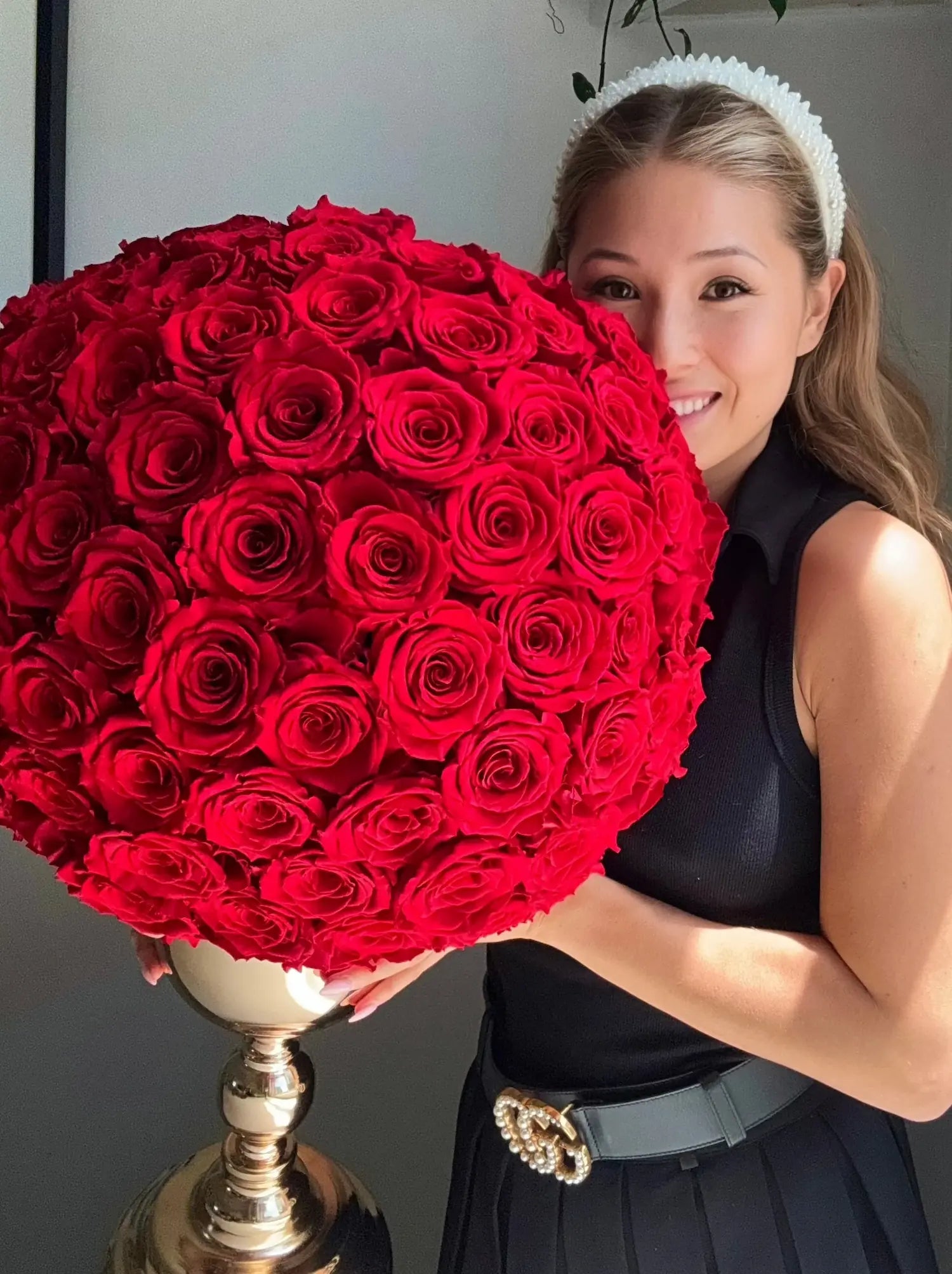 Woman holding a large bouquet of red roses on a gold stand.