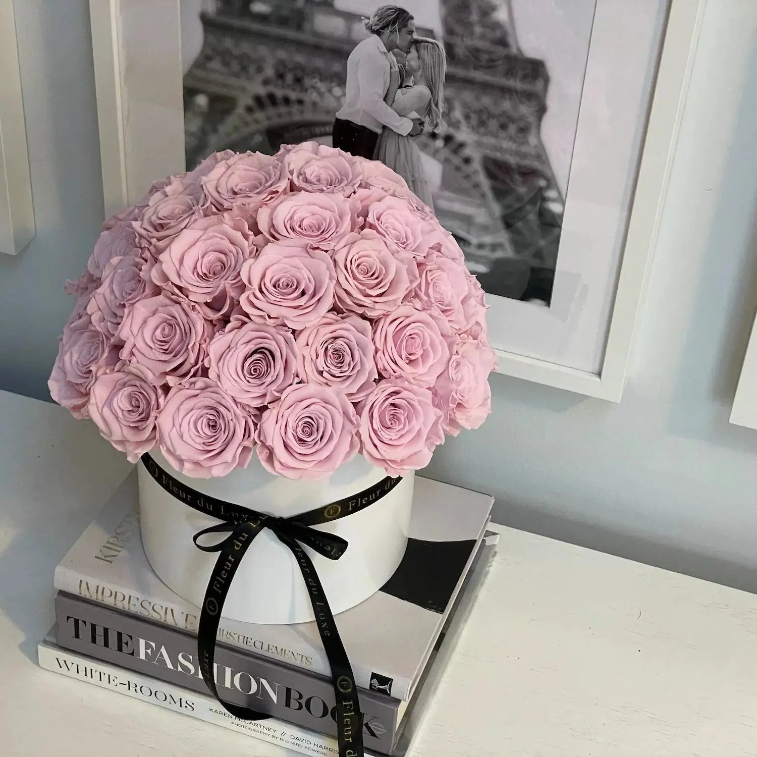 Pink rose bouquet in a white container on books with a framed picture of the Eiffel Tower in the background.