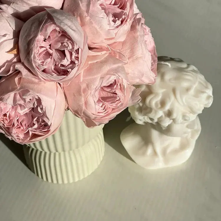 Pink flowers in a vase next to a white decorative bust on a light surface