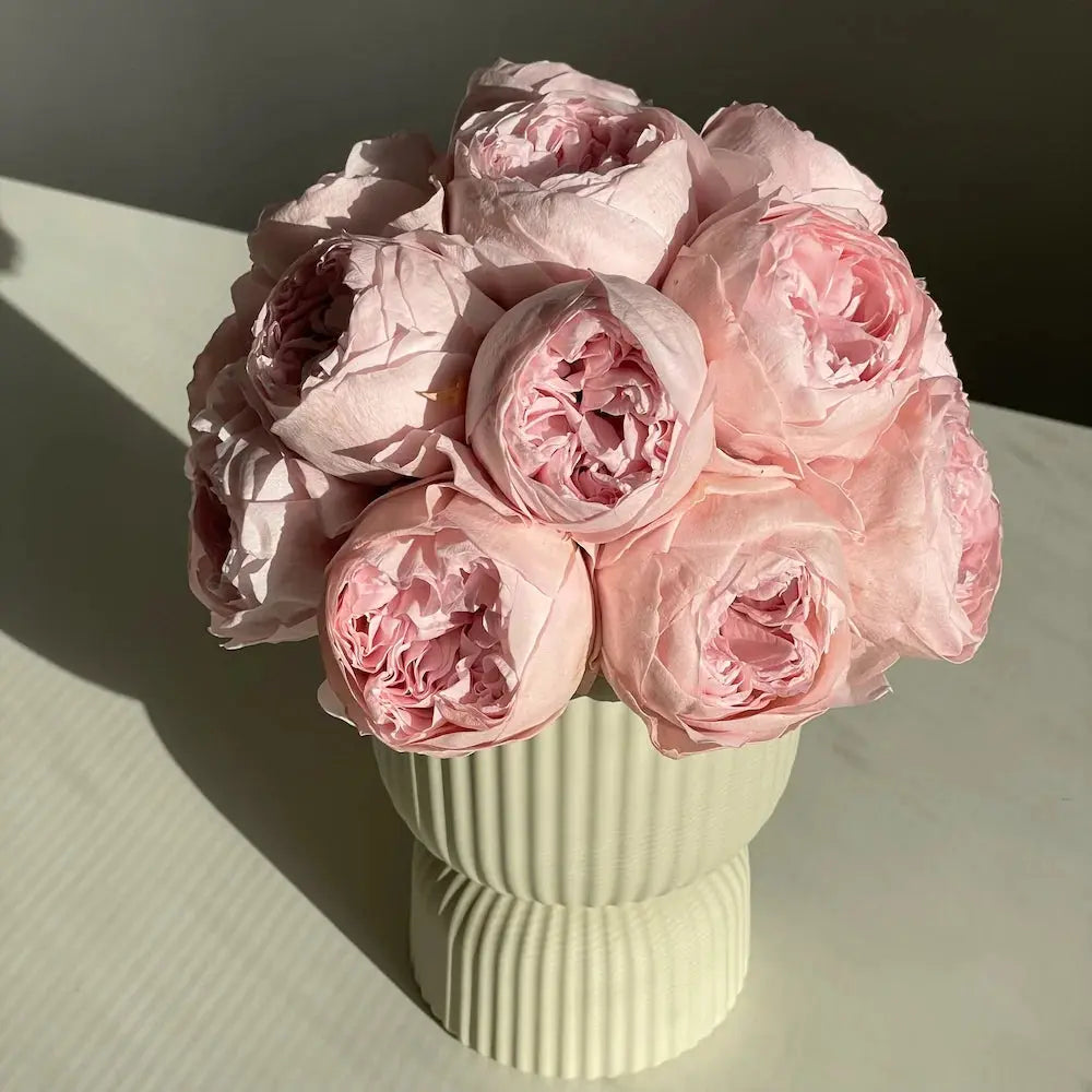 Bouquet of pink roses in a green vase on a light surface with a dark background