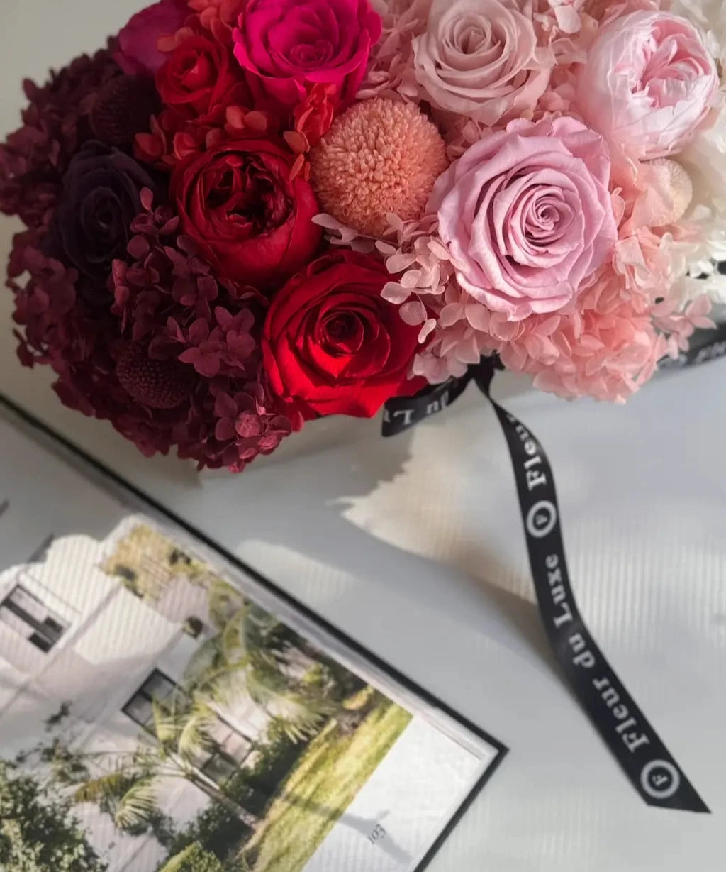 Bouquet of red and pink flowers on a white surface with a black ribbon.